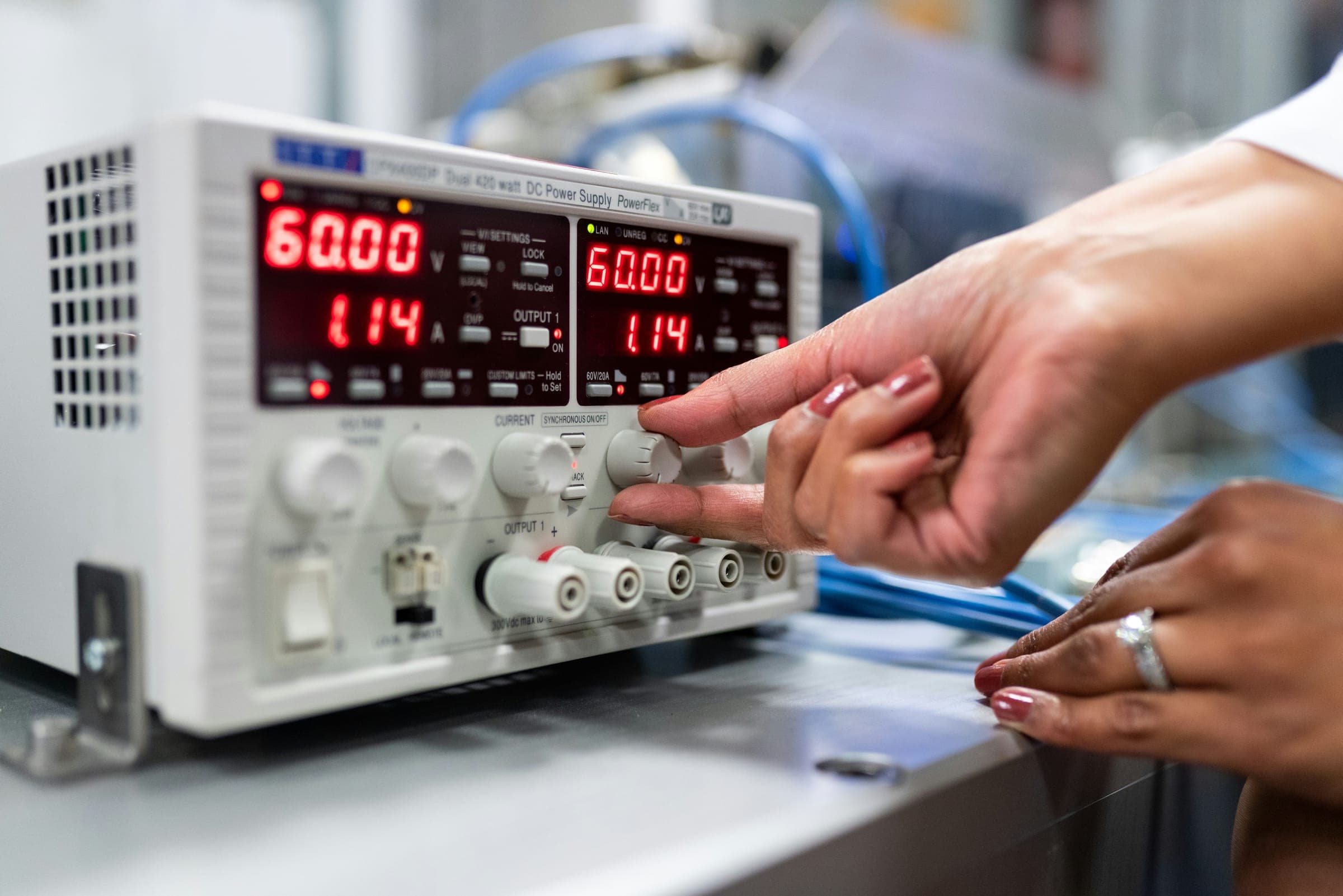 A technician's hands adjusting the controls of a lab bench power supply