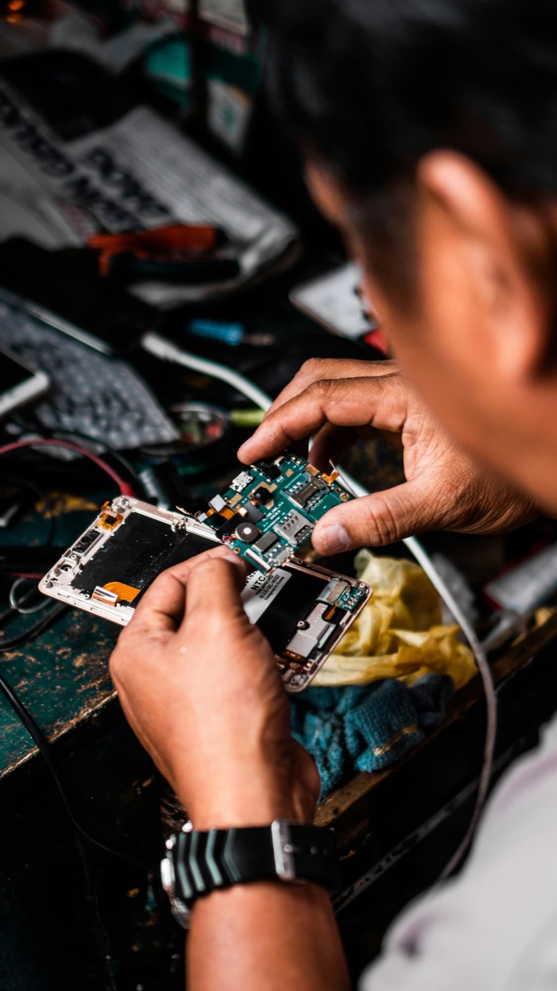 Close-up of hands repairing a disassembled phone's internal circuit board
