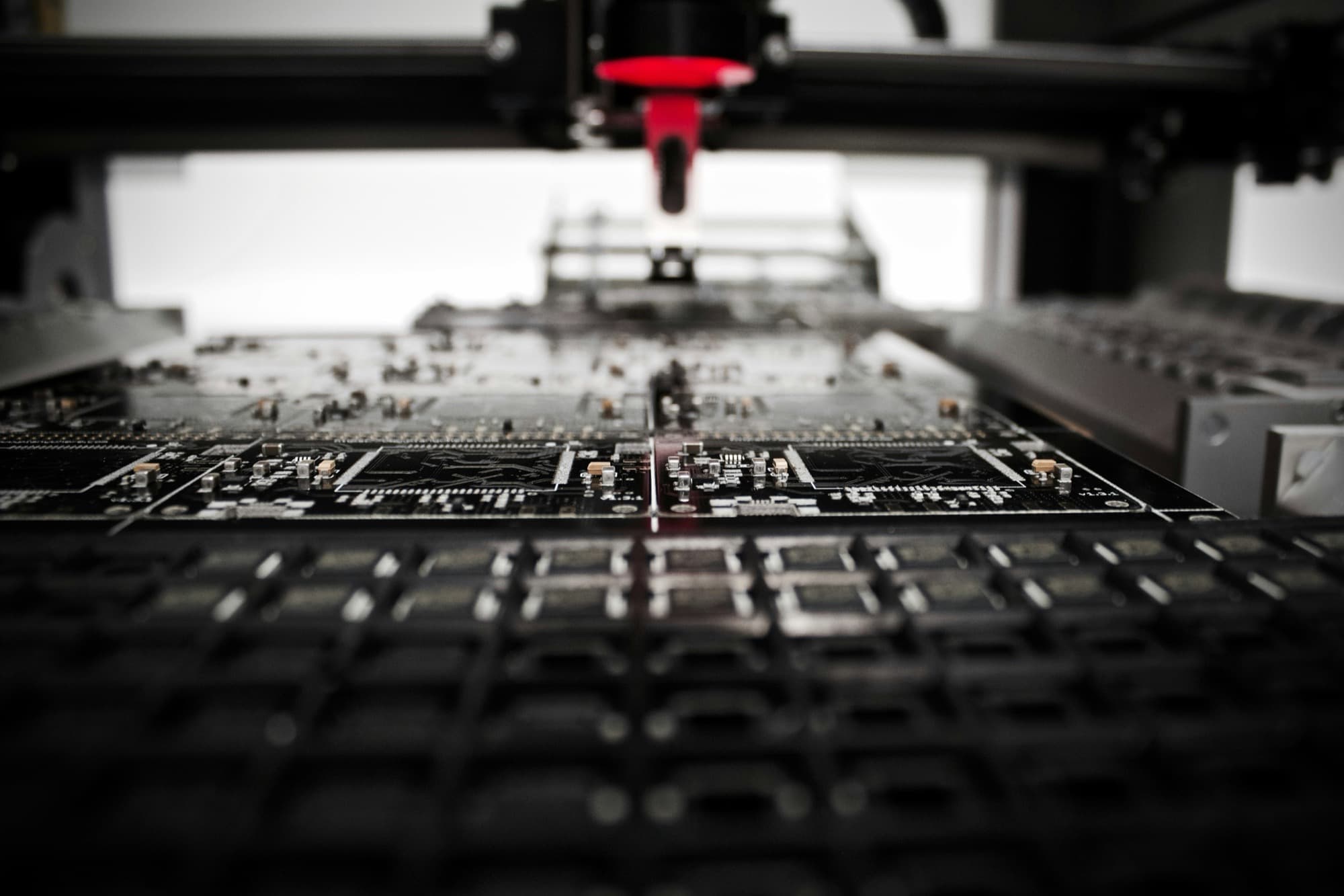 Close-up of a pick-and-place machine over a panel of populated circuit boards